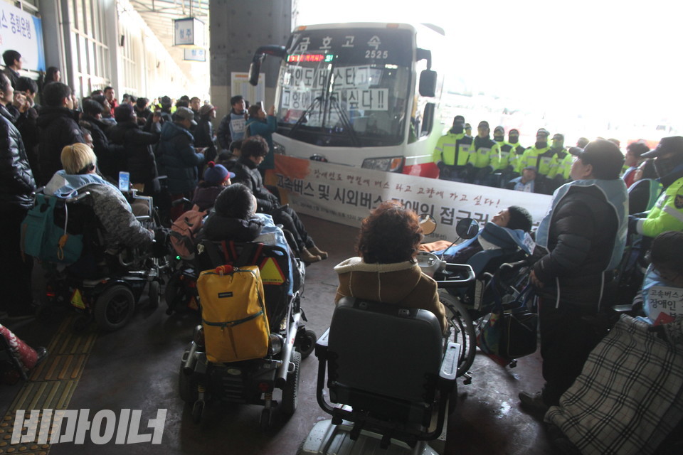 장애인들이 버스를 막고 '장애인도 버스타고 고향에 가고 싶다!'를 붙이고 있다.